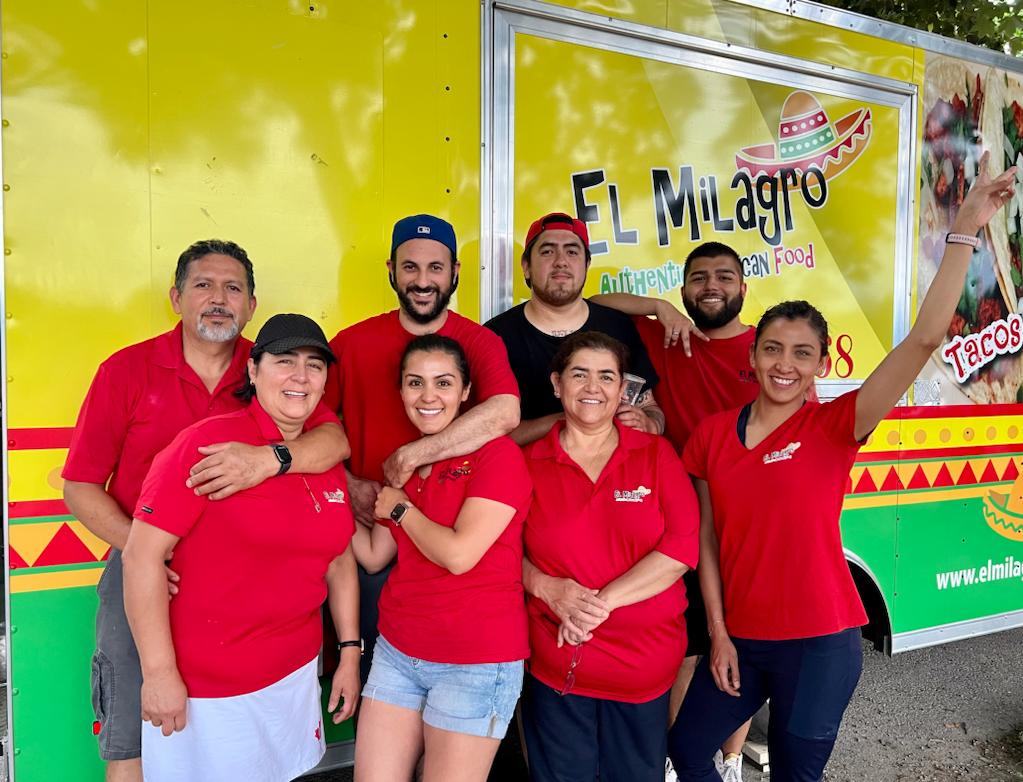 El Milagro team of 8 picture with their uniform and the yellow trailer behind.